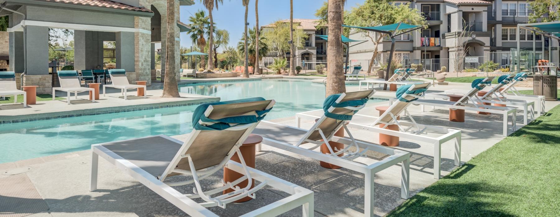 a pool with lounge chairs on sundeck and palm trees